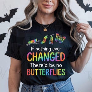 Puede incluir: Camiseta negra con un gráfico colorido de una oruga transformándose en mariposa. La camiseta presenta el texto "If nothing ever CHANGED There'd be no BUTTERFLIES" en colores arcoíris. El diseño incluye una oruga, crisálida y mariposa.