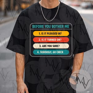 Peut inclure: T-shirt noir avec le texte "BEFORE YOU BOTHER ME" et une liste de contrôle : "1. IS IT PLUGGED IN ?", "2. IS IT TURNED ON ?", "3. ARE YOU SURE ?" et "4. SERIOUSLY, GO CHECK". Le texte est en blanc, jaune, rouge et sarcelle.