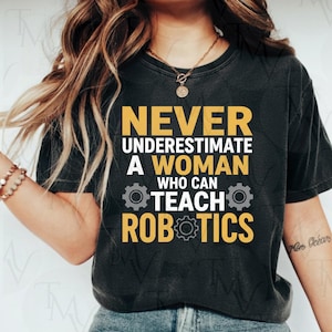 Peut inclure: T-shirt gris foncé avec le texte "NEVER UNDERESTIMATE A WOMAN WHO CAN TEACH ROBOTICS" en jaune et blanc. Le design comprend des icônes d'engrenages. Un vêtement décontracté.
