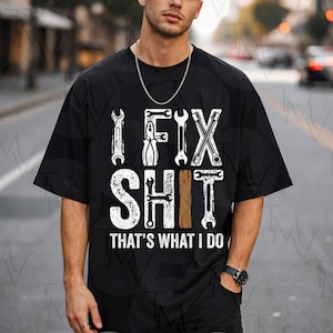 Puede incluir: Camiseta negra con la frase "I FIX SHIT THAT'S WHAT I DO" en blanco y marrón. El diseño incorpora gráficos de llaves y herramientas. Una camiseta casual de manga corta para mecánicos y aficionados al bricolaje.
