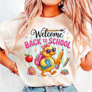 Peut inclure: Un t-shirt couleur crème avec un motif représentant un caneton jaune portant des lunettes de soleil roses et un nœud à pois roses. Le caneton porte un sac à dos rose et un livre bleu marqué ABC's, tenant un grand crayon. Texte : Welcome BACK TO SCHOOL.