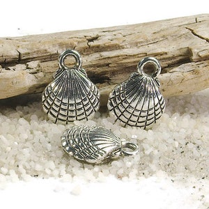 Puede incluir: Tres abalorios de metal plateados con forma de conchas marinas. Los abalorios tienen un diseño detallado y un bucle en la parte superior para sujetarlos a joyas u otras manualidades.