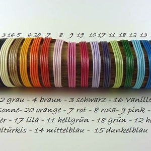 Pode incluir: Uma fila de 15 cordões de diferentes cores, numerados de 1 a 15, com uma descrição de cada cor abaixo. Os cordões estão dispostos sobre uma superfície de madeira.