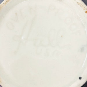 May include: Close-up of the base of a ceramic vase with a black glaze. The base is marked with the text "S.F. Hale" in black.