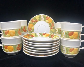 May include: A set of six white ceramic teacups and saucers with a fruit design. The cups and saucers feature a yellow, orange, and green pattern of fruit and leaves.