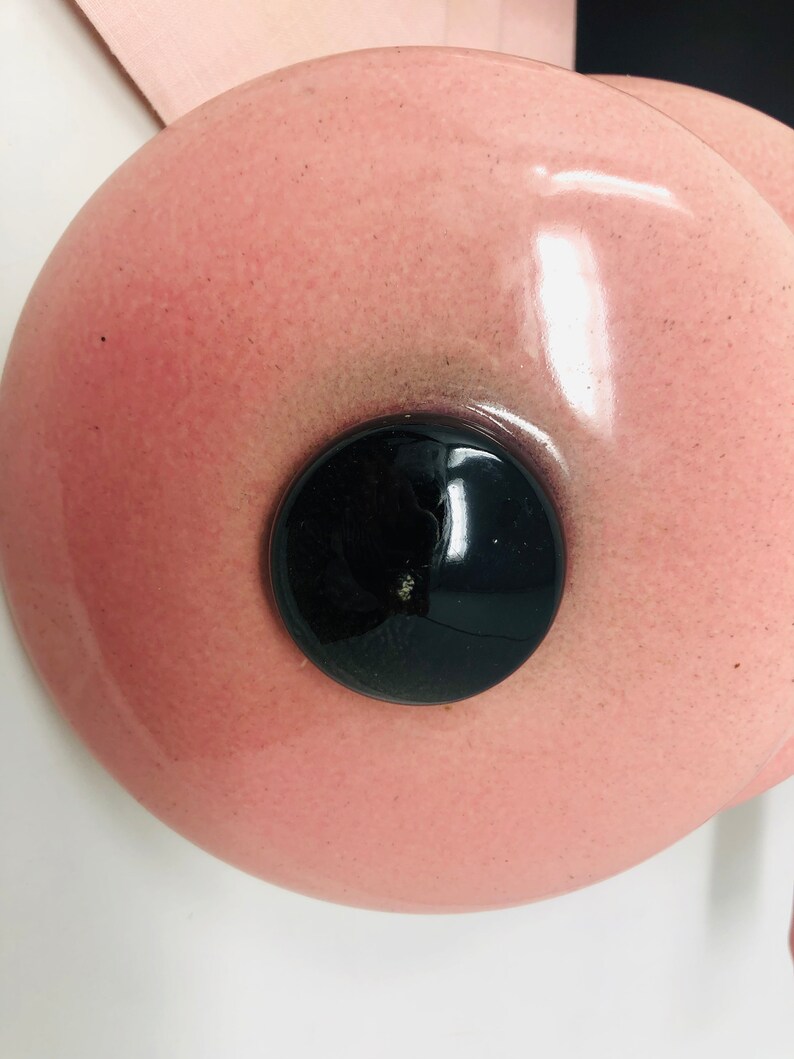 May include: A pink ceramic lid with a black circular knob in the centre. The lid has a glossy finish and a speckled texture.