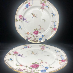 May include: Two white ceramic dinner plates with a gold rim and a floral pattern in shades of pink, blue, and yellow.