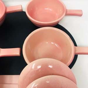 May include: Set of pink ceramic bowls with handles. The bowls are stacked on top of each other.
