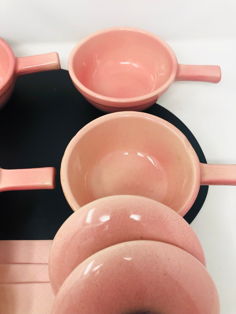 May include: Set of pink ceramic bowls with handles. The bowls are stacked on top of each other.