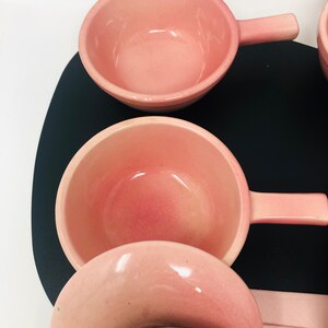 May include: Set of four pink ceramic bowls with handles. The bowls are nested inside each other, with the largest bowl at the top and the smallest bowl at the bottom.