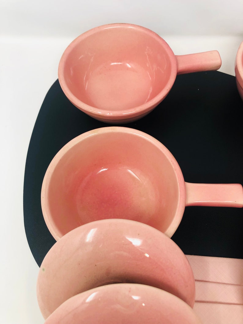 May include: Set of four pink ceramic bowls with handles. The bowls are nested inside each other, with the largest bowl at the top and the smallest bowl at the bottom.