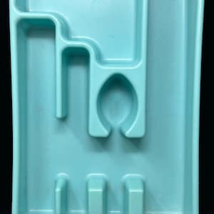 May include: A rectangular light blue plastic cutlery tray featuring multiple molded compartments of varying shapes and sizes designed for organizing silverware, including a central rounded section and several smaller slots.