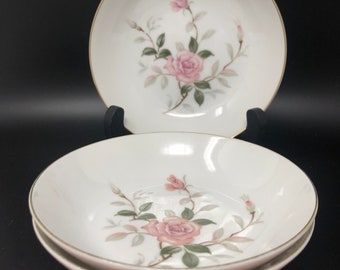 May include: Three white ceramic bowls with a delicate floral design featuring pink roses and green leaves. The bowls have a gold rim and are stacked on top of each other.