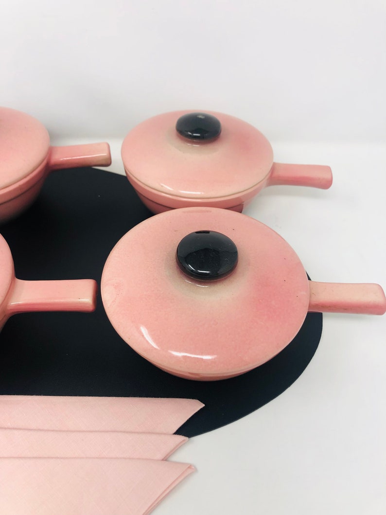 May include: Set of four pink ceramic individual serving dishes with lids and black handles. Each dish has a black knob on the lid.