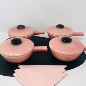 May include: Set of four pink ceramic ramekins with black handles and lids. The ramekins are on a black tray with a pink napkin.