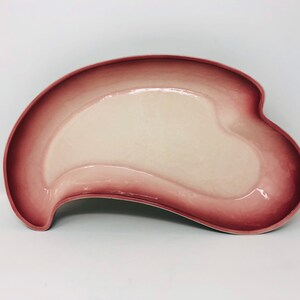 May include: A pink and white ceramic serving dish with a unique, asymmetrical shape. The dish has a smooth, glossy finish.