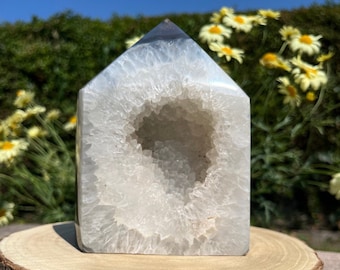 May include: White agate crystal with a large, open geode cavity. The crystal is shaped like a pyramid and has a smooth, polished surface.