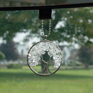 May include: A silver chain with a crystal tree of life pendant hanging from a rear view mirror. The tree is made of clear crystals and silver wire.