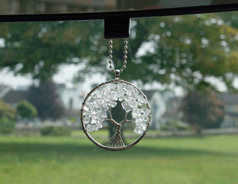 May include: A silver chain with a crystal tree of life pendant hanging from a rear view mirror. The tree is made of clear crystals and silver wire.