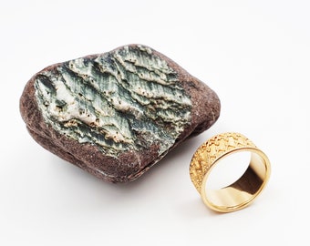 May include: A gold ring with a textured surface and a rough, brown and green rock.