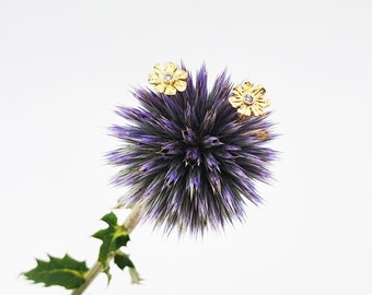 May include: A purple thistle with two gold flower-shaped earrings with clear stones.