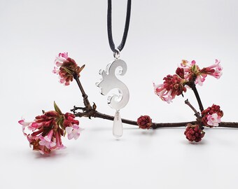 May include: A silver pendant necklace with a delicate, swirling design and a pearlescent drop. The necklace is displayed on a branch with pink flowers.