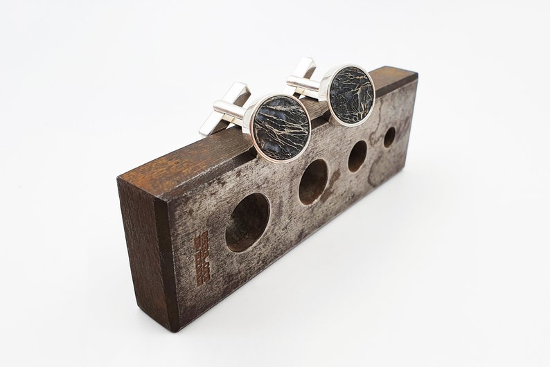 Puede incluir: Un par de gemelos de plata con incrustaciones circulares negras en un expositor de madera.