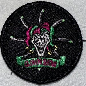 May include: A black and green embroidered patch with a white jester face and the text "Clown Show".