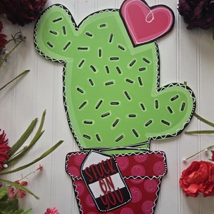 May include: A green cactus with black dots and a pink heart on top, in a red pot with white polka dots and a tag that says "Stuck on You".