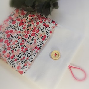 Puede incluir: Una peque&ntilde;a bolsa blanca con un estampado floral rosa en la solapa delantera. La bolsa tiene un cierre de bot&oacute;n &uacute;nico y un lazo el&aacute;stico rosa.