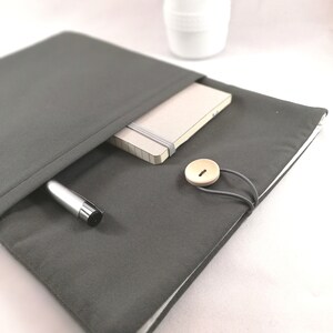 May include: A gray fabric zippered pouch with a pen and notebook inside. The pouch has a wooden button closure and a white lining.