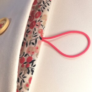 Puede incluir: Una bolsa de tela blanca con un lazo el&aacute;stico rosa. La bolsa tiene un forro de estampado floral con detalles rojos y negros.