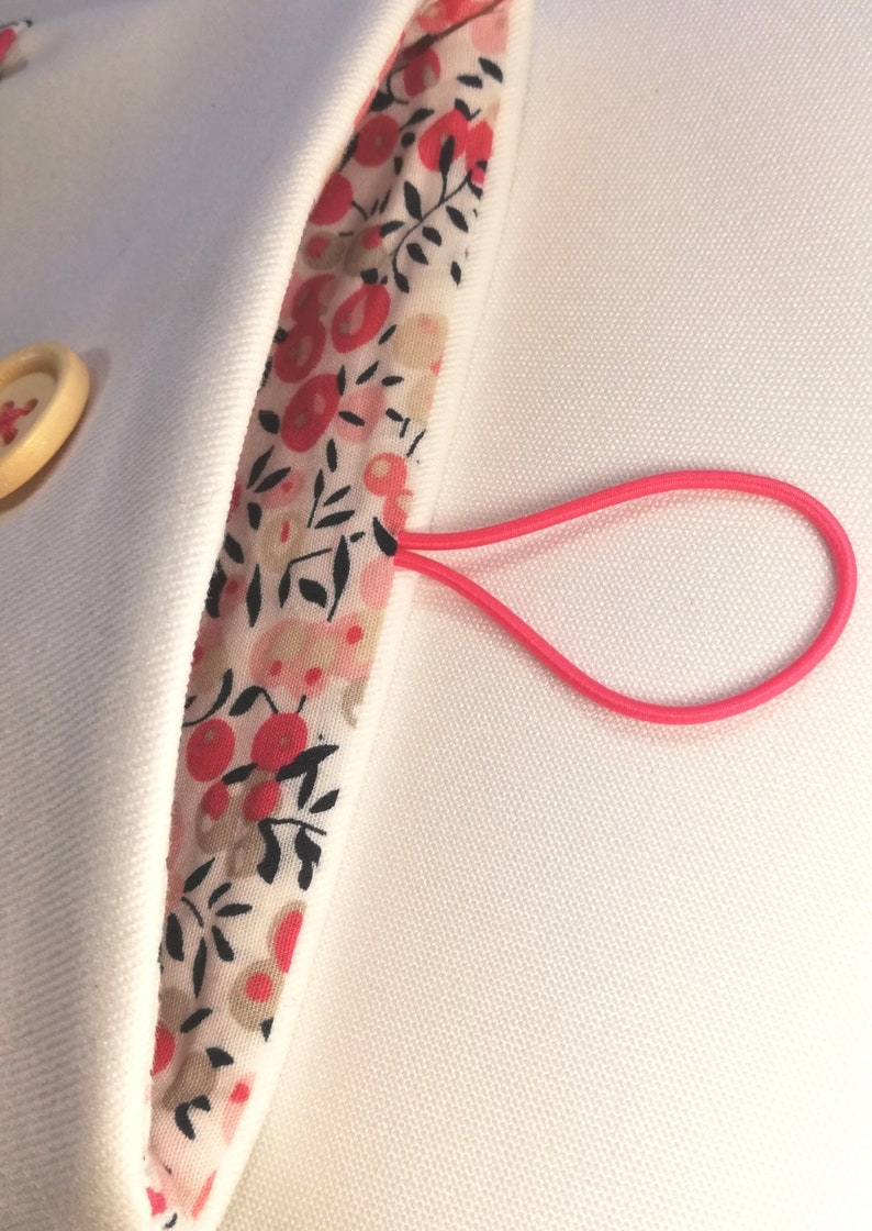 Puede incluir: Una bolsa de tela blanca con un lazo el&aacute;stico rosa. La bolsa tiene un forro de estampado floral con detalles rojos y negros.