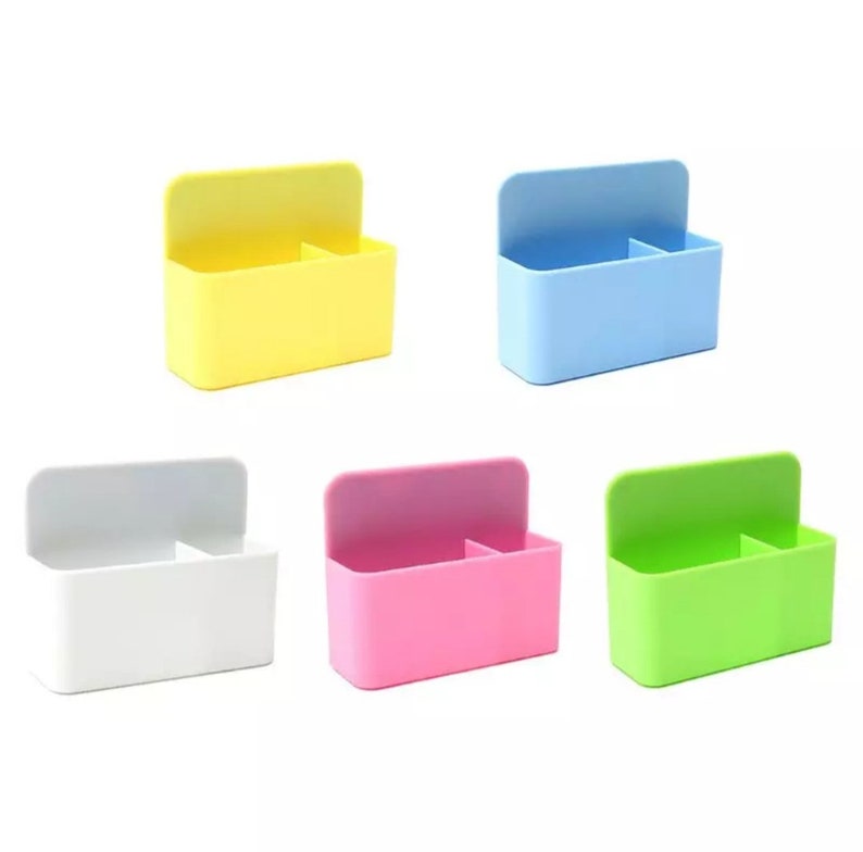 May include: A collection of five colorful plastic organizers. Each organizer has a rectangular body with a divided interior and a hinged lid. The colors include yellow, blue, white, pink, and green. The organizers are designed for desk or storage use.
