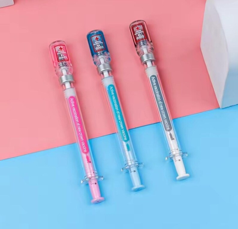 May include: Three syringe-shaped pens with clear barrels and colorful accents. Each pen has a different colored plunger: pink, blue, and red. The pens have the text "COVID 19" and "Active vaccination of new crown vaccine."