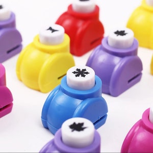 May include: A set of colorful paper punchers with different designs, including a snowflake, a leaf, and a star. The punchers are made of plastic and have a white handle.