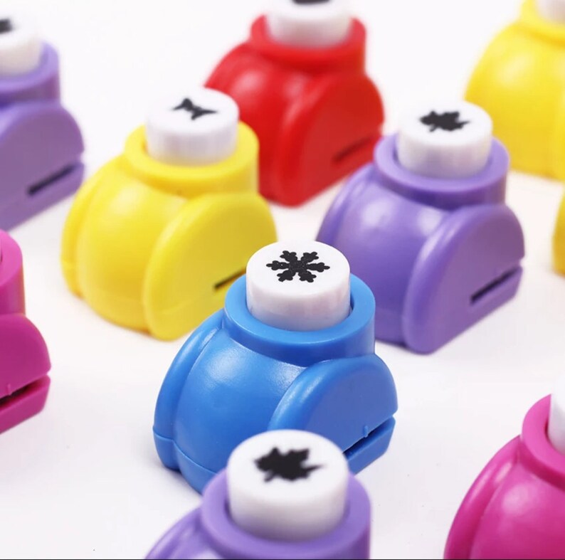 May include: A set of colorful paper punchers with different designs, including a snowflake, a leaf, and a star. The punchers are made of plastic and have a white handle.
