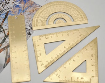 May include: A set of four gold-toned metal rulers, including a protractor, a 10-inch ruler, and two triangles. The rulers are marked in centimeters.