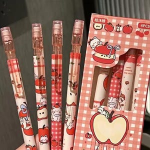 May include: A set of four pens with a red and white apple theme. The pens have a clear top and are decorated with apple and cat illustrations. The packaging features a red and white checkered pattern and apple graphics.