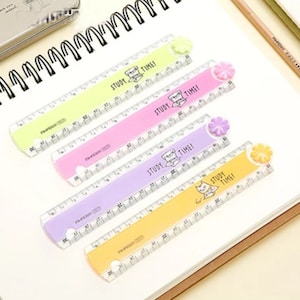 May include: Four plastic rulers in lime green, pink, lavender, and yellow, each featuring a small flower-shaped knob at one end. The rulers are printed with the text STUDY TIME! and a small cat illustration, with clear measurement markings.
