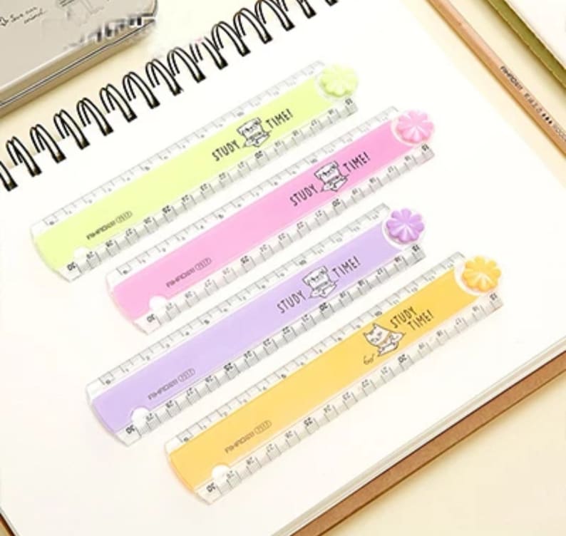 May include: Four plastic rulers in lime green, pink, lavender, and yellow, each featuring a small flower-shaped knob at one end. The rulers are printed with the text STUDY TIME! and a small cat illustration, with clear measurement markings.