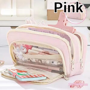 May include: A light pink multi-compartment pencil case with a zippered opening. The interior features a mesh pocket containing pens and a small notebook with a cherry illustration. The text "Pink" appears at the top, and "210*150*90mm" is visible.