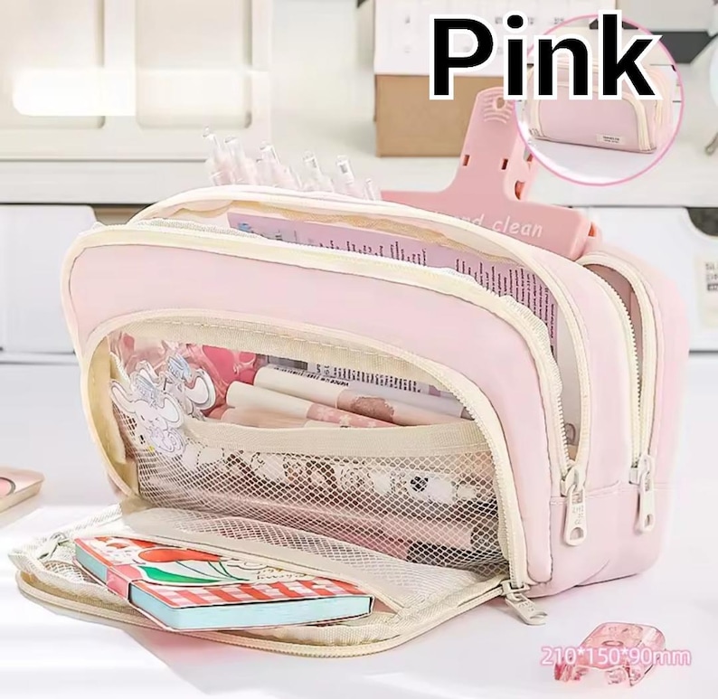 May include: A light pink multi-compartment pencil case with a zippered opening. The interior features a mesh pocket containing pens and a small notebook with a cherry illustration. The text "Pink" appears at the top, and "210*150*90mm" is visible.