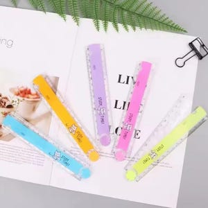 May include: Five plastic rulers in blue, yellow, purple, pink, and lime green. Each ruler features a clear edge with measurement markings and a solid coloured centre strip printed with a cartoon cat and the text STUDY TIME in black ink.
