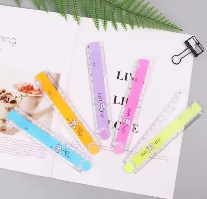 May include: Five plastic rulers in blue, yellow, purple, pink, and lime green. Each ruler features a clear edge with measurement markings and a solid coloured centre strip printed with a cartoon cat and the text STUDY TIME in black ink.