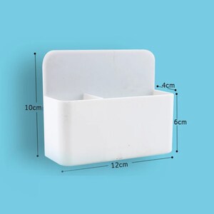 May include: A white plastic wall-mounted organizer with two compartments. The organizer is 12 cm wide, 10 cm tall, and 4 cm deep. It is designed to hold small items and has a simple, clean design.
