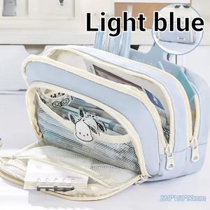 May include: A light blue multi-compartment pencil case with white zippers and trim. The front features a mesh pocket with a cartoon character graphic and a small notebook. The dimensions are printed as 210*150*90mm. The text Light blue is visible.