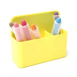May include: A yellow plastic container holding several colorful crayons. The crayons are in various colors, including pink, orange, blue, and purple. The container is divided into sections.