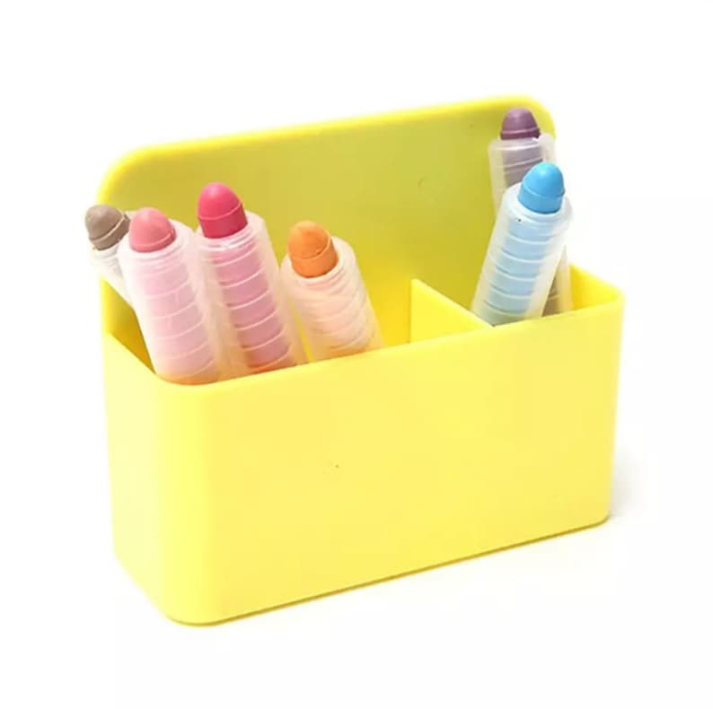 May include: A yellow plastic container holding several colorful crayons. The crayons are in various colors, including pink, orange, blue, and purple. The container is divided into sections.
