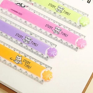May include: Four plastic rulers in lime green, pink, purple, and yellow, each featuring a cartoon animal illustration and the text "STUDY TIME!". Each ruler has a flower-shaped knob at one end and clear measurement markings in centimetres.